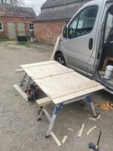 A wooden door being made next to a silver van