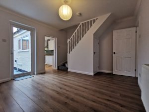 A room with a wooden floor and doorway through to a kitchen