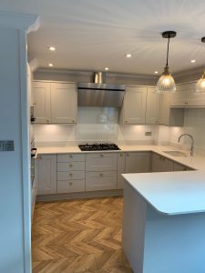 A beautiful kitchen with grey cupboards, gold handles, white worktop and parquet floor