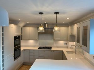 A beautiful kitchen with grey cupboards, gold handles, white worktop and parquet floor