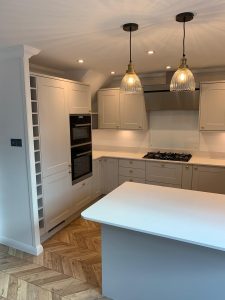 A beautiful kitchen with grey cupboards, gold handles, white worktop and parquet floor