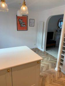 A beautiful kitchen with grey cupboards, gold handles, white worktop and parquet floor
