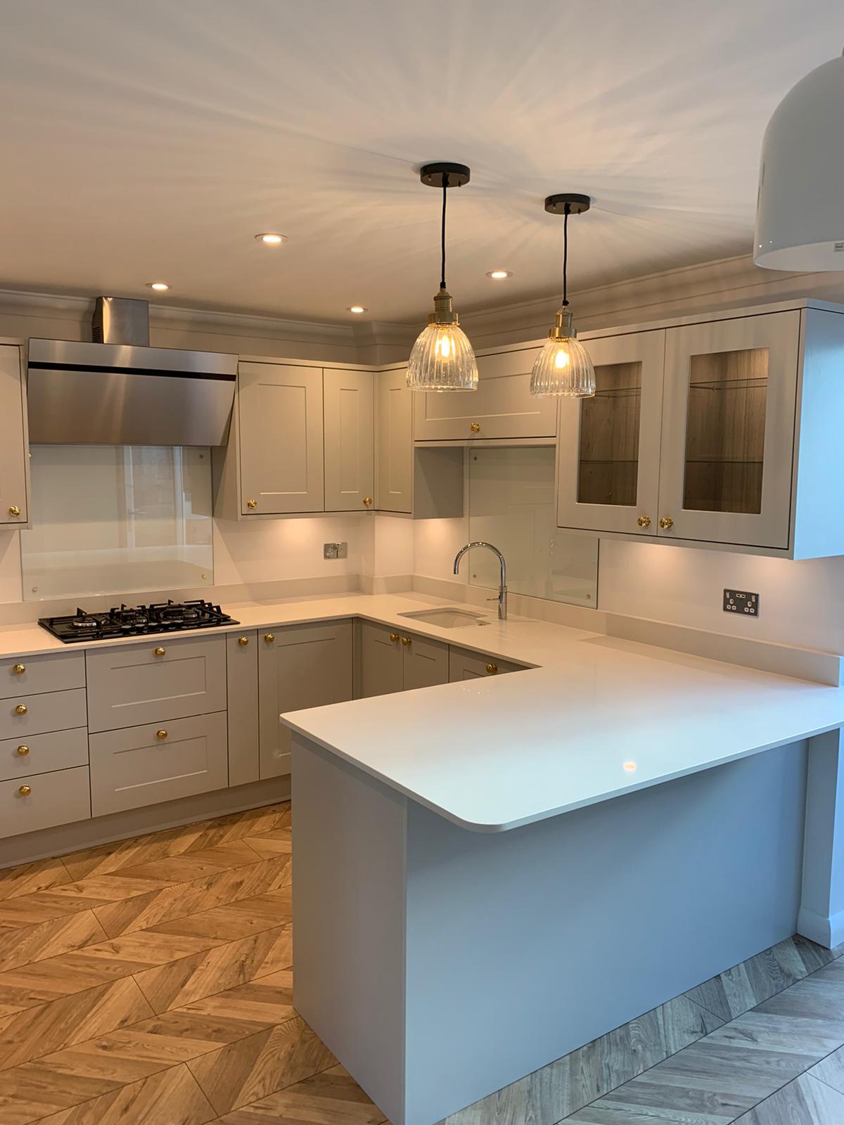 A beautiful kitchen with grey cupboards, gold handles, white worktop and parquet floor