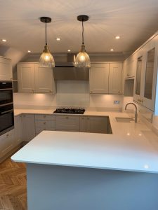 A beautiful kitchen with grey cupboards, gold handles, white worktop and parquet floor