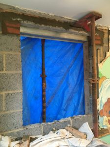 A breeze block room with tarpaulins covering a gap